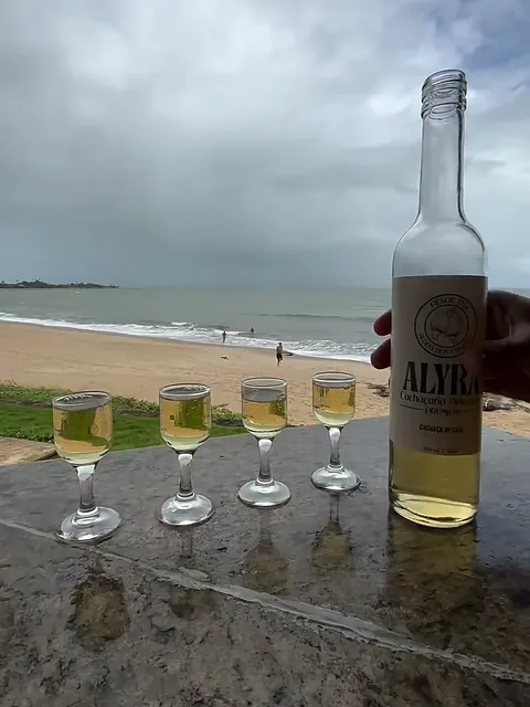Quatro cálices com ALYRA numa mesa de granito, com a praia ao fundo