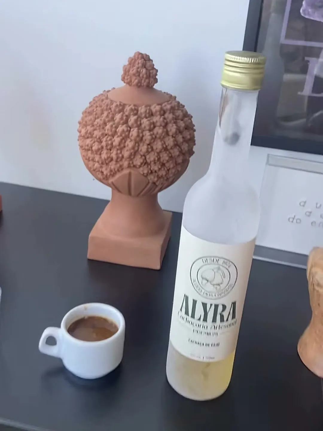 Garrafa gelada de ALYRA, suada de tão fria, ao lado de uma xícara de caldinho