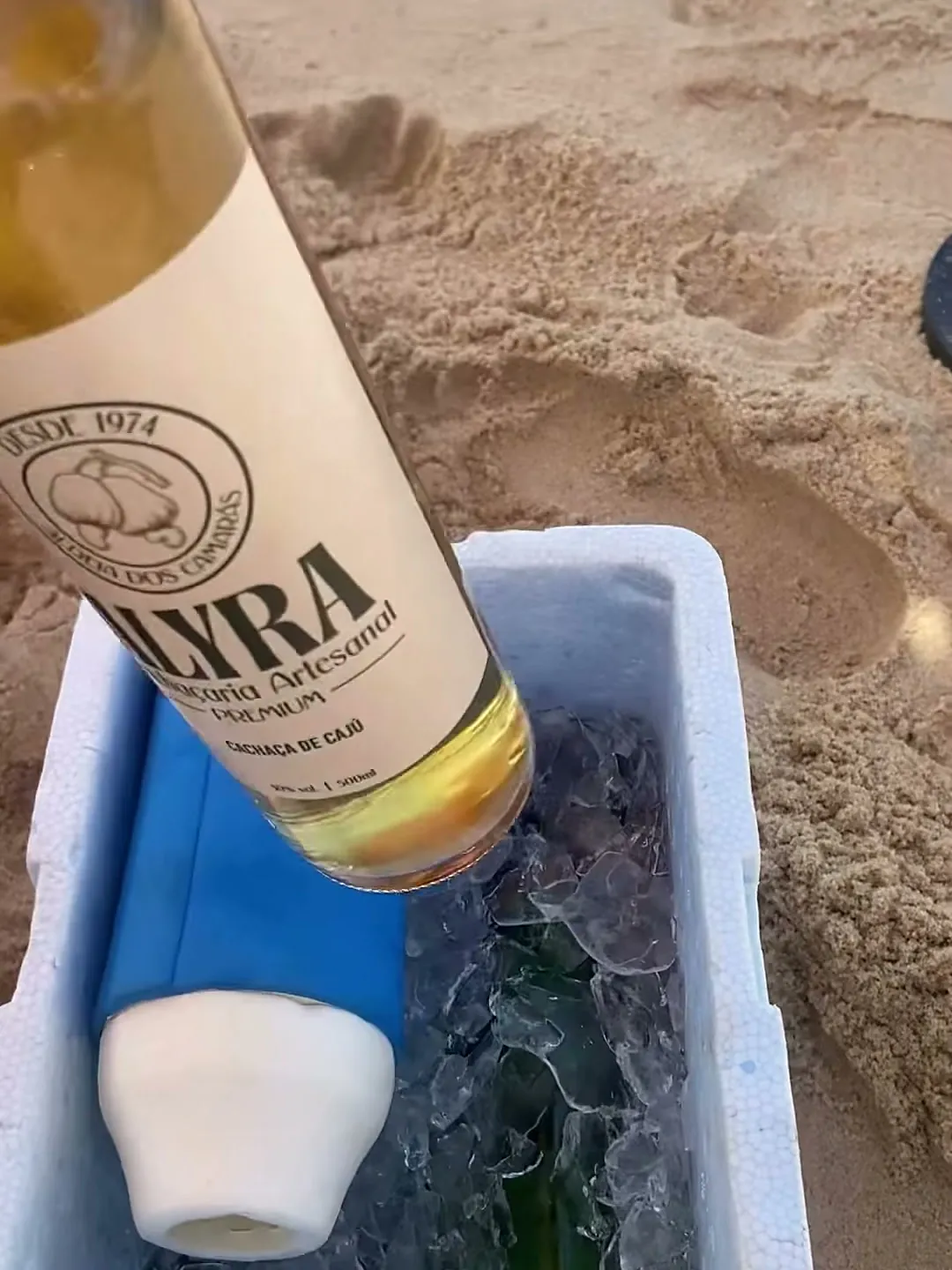 Garrafa de ALYRA saindo da caixa de isopor com gelo, na praia